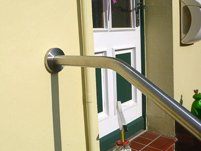 Edelstahl Handlauf freistehend gebogen in der Form 3 - 2 Bögen - an einer Eingangstreppe auf der Nordseeinsel Wangerooge - Befestigung  an der Hauswand mit einer Edelstahlronde mit integriertem Gummiring, damit die Abdeckrosette nicht abklappen kann